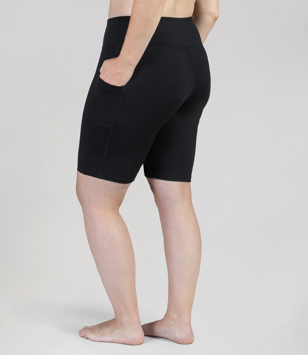Plus size woman, back view, wearing JunoActive JunoStretch Side Pocket Short in black. The hem is a few inches above the knee.