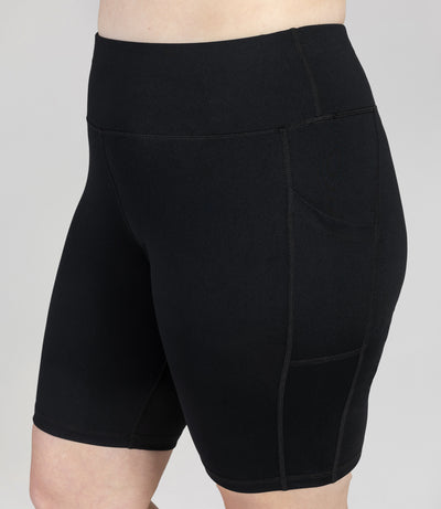 Plus size woman, front view, close up of wearing JunoActive JunoStretch Side Pocket Short in black. The hem is a few inches above the knee.
