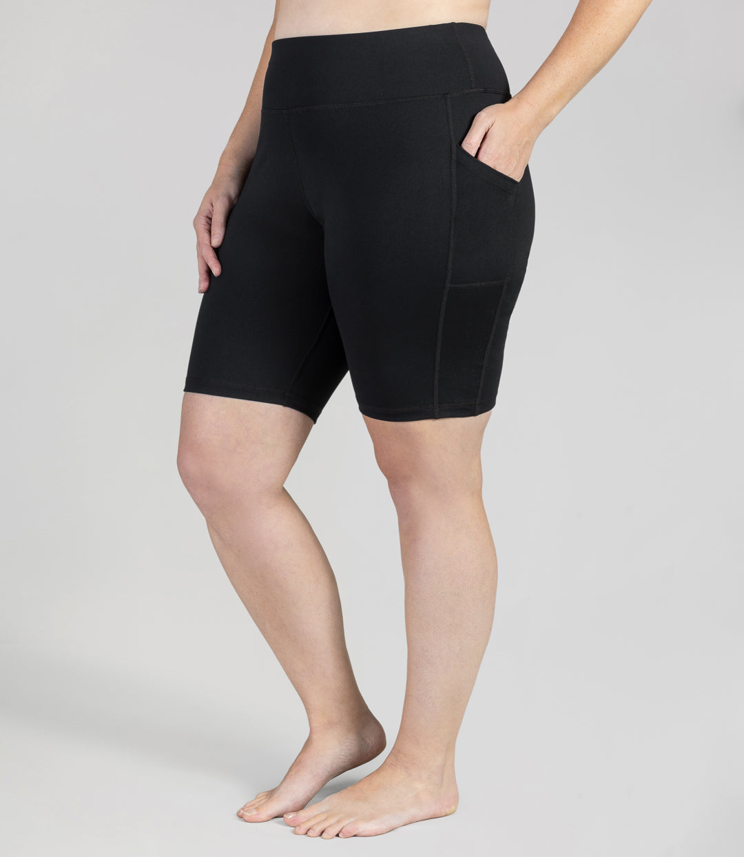 Plus size woman, front view, wearing JunoActive JunoStretch Side Pocket Short in black. The hem is a few inches above the knee.