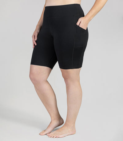 Plus size woman, front view, wearing JunoActive JunoStretch Side Pocket Short in black. The hem is a few inches above the knee.