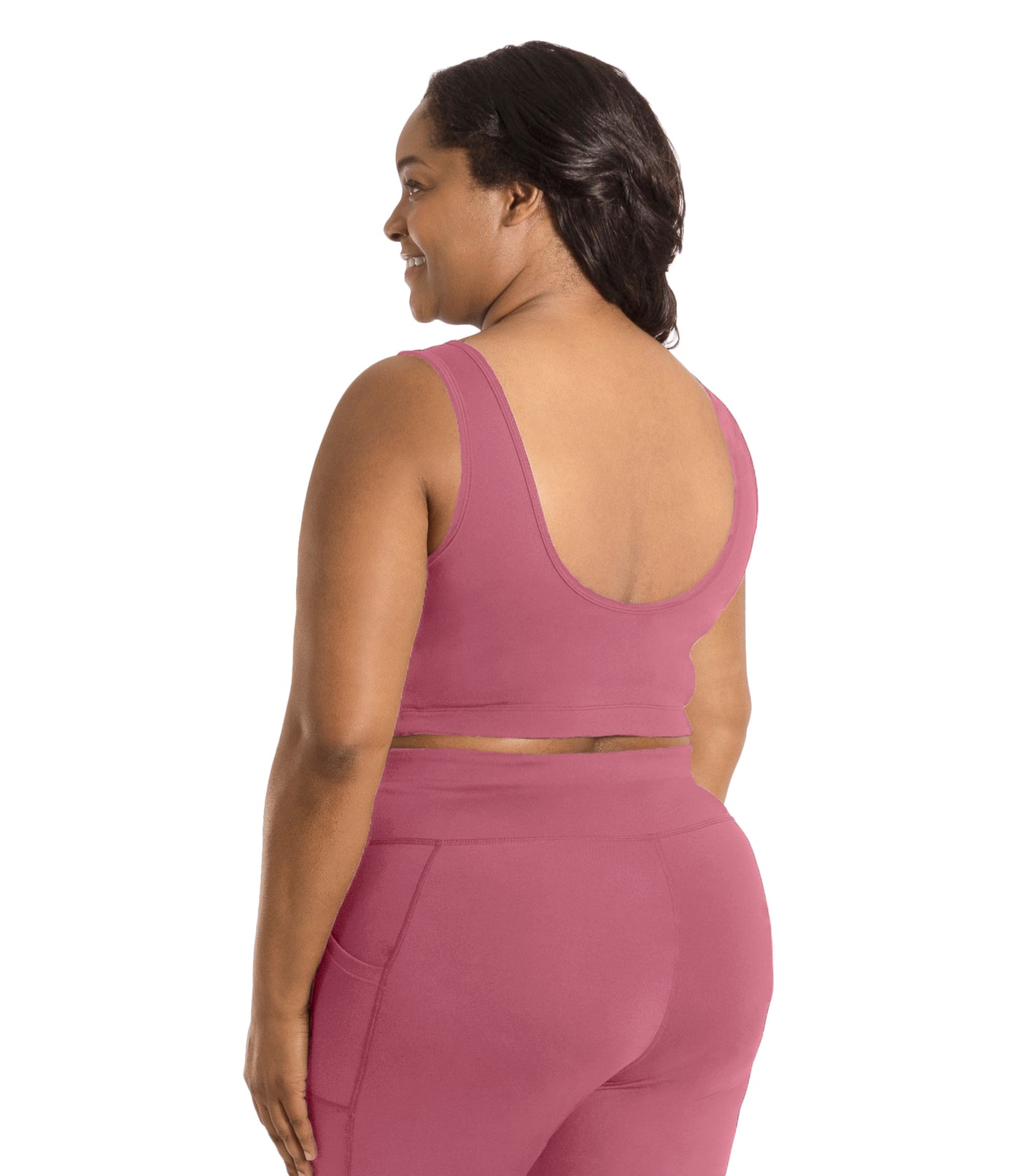 Plus size woman, facing back, wearing JunoActive plus size JunoStretch Scoop Bra in mauve. The woman is wearing black plus size JunoActive leggings. Her arms fall naturally to her side with her hands on her thighs.