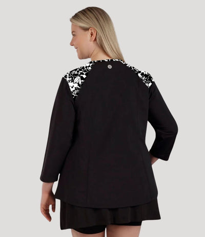 Plus size woman, facing back, wearing QuikEnergy ¾ Sleeve Swim and Sun Top Black and hibiscus print on shoulders and solid black colorblocking on the sleeves and torso.