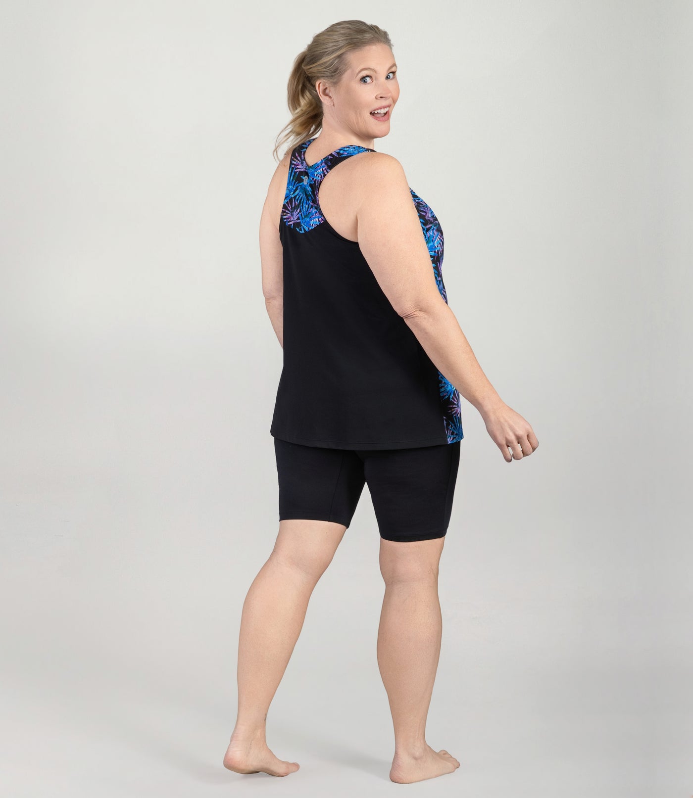Plus size model, facing back with head turned front looking at camera, wearing AquaSport Hanalei Plus size Tankini Top Jewel Palmetto Print.
