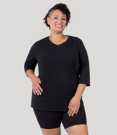 Plus size woman, facing front, wearing JunoActive's Aquasport 3/4 Sleeve Plus size Rash Guard in color black.