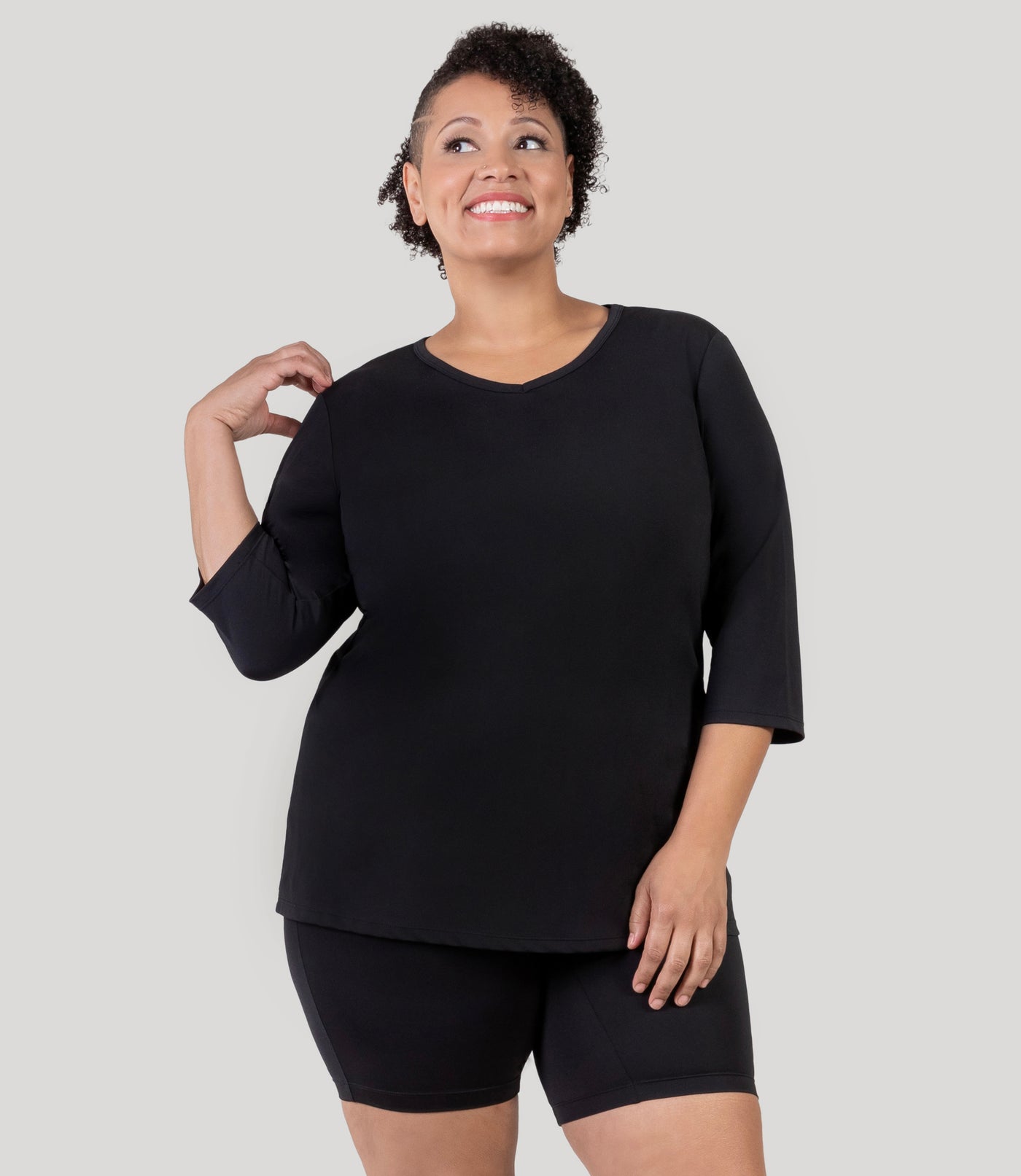 Plus size woman, facing front with hand on her shoulder, wearing JunoActive's Aquasport 3/4 Sleeve Plus size Rash Guard in color black.