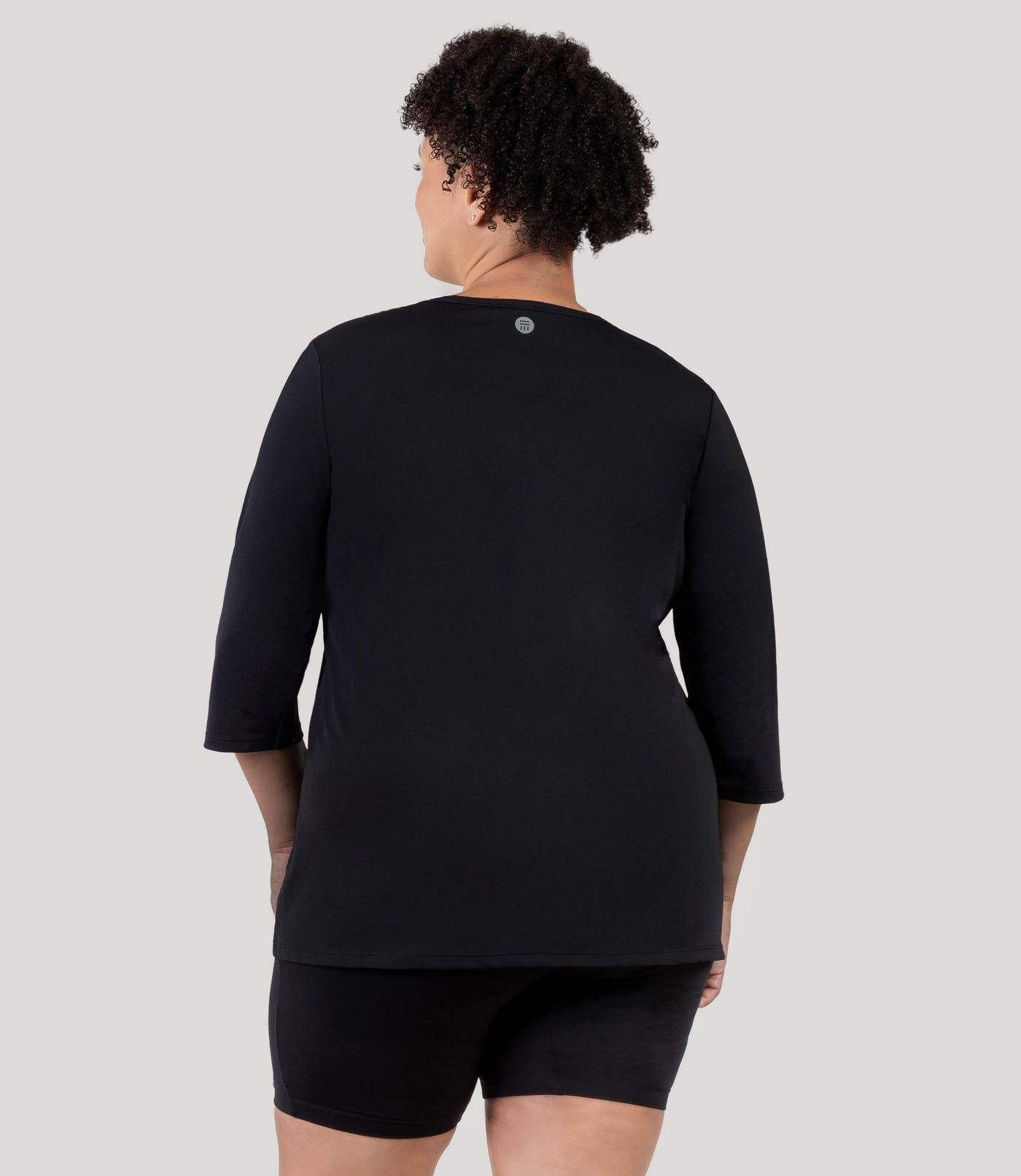 Plus size woman, facing back, wearing JunoActive's Aquasport 3/4 Sleeve Plus size Rash Guard in color black.