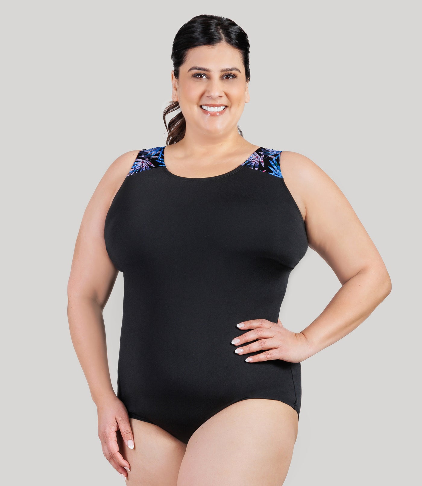Plus size model, facing front, wearing JunoActive's AquaSport Crossback Plus Size Tanksuit in Black and Jewel Palmetto print.