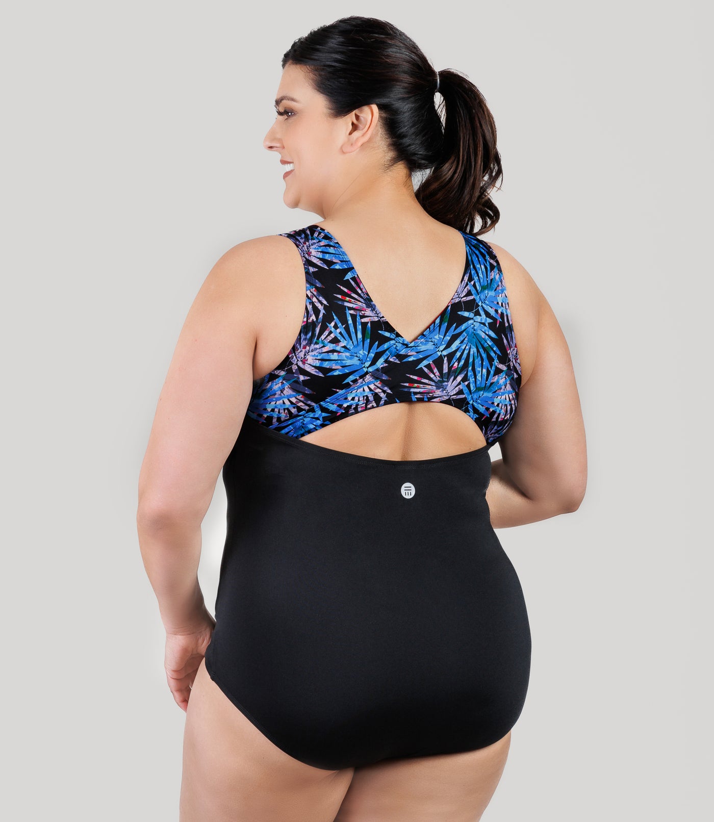 Plus size model, facing back, wearing JunoActive's AquaSport Crossback Plus Size Tanksuit in Black and Jewel Palmetto print.