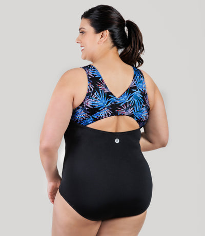 Plus size model, facing back, wearing JunoActive's AquaSport Crossback Plus Size Tanksuit in Black and Jewel Palmetto print.
