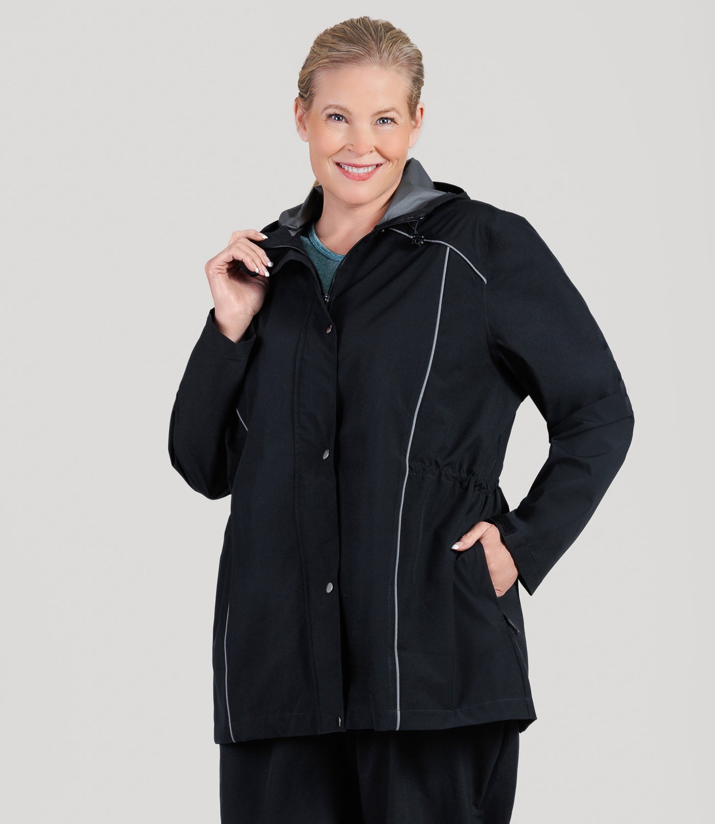 Plus size model, wearing JunoActive's Adventure Wind and Rain Jacket in color black. Her left hand is in her pocket and right hand is gently holding the collar of jacket.