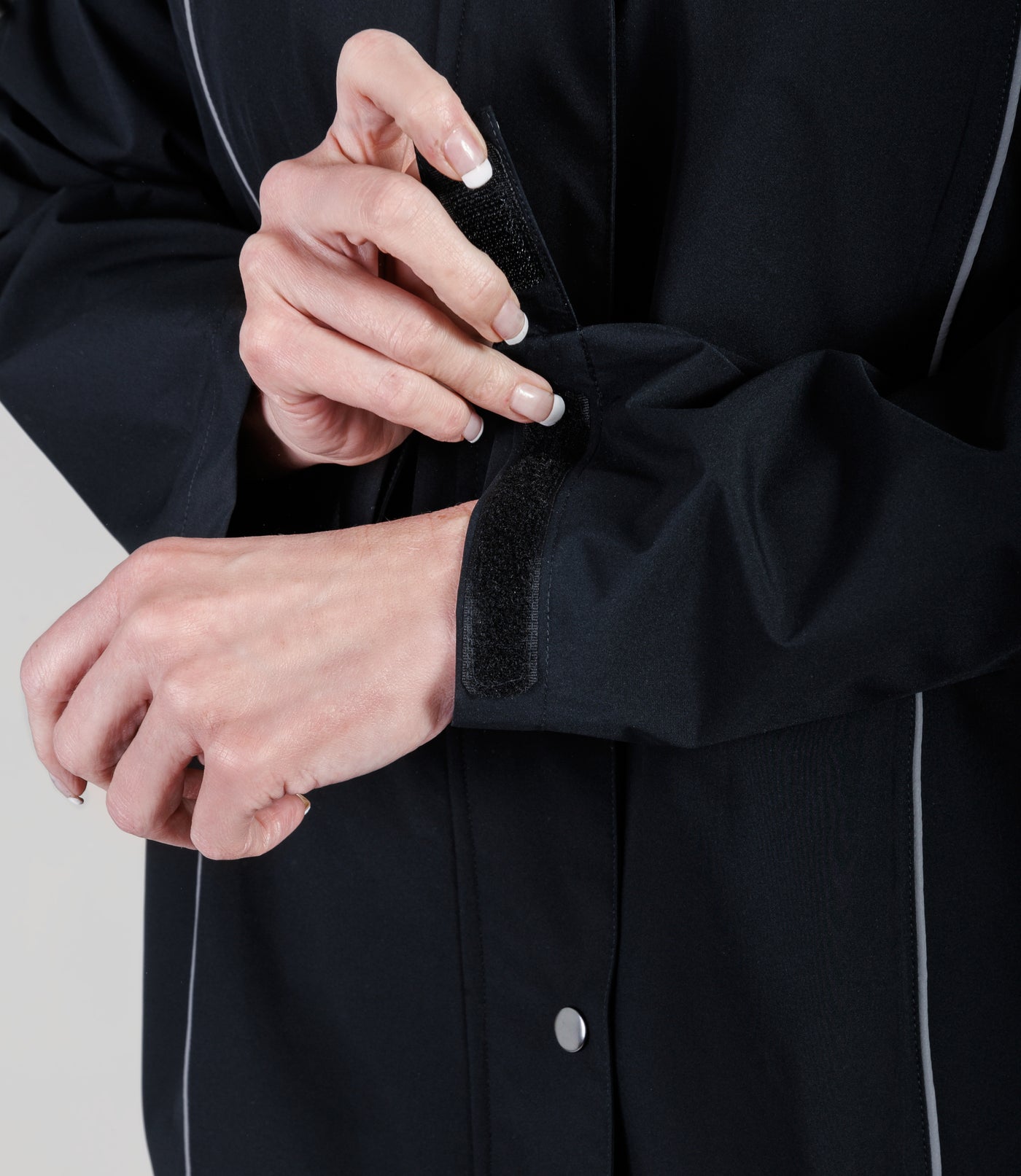 Plus size model, wearing JunoActive's Adventure Wind and Rain Jacket in color black, close up of model wrapping the velcro of the arm of jacket featured.