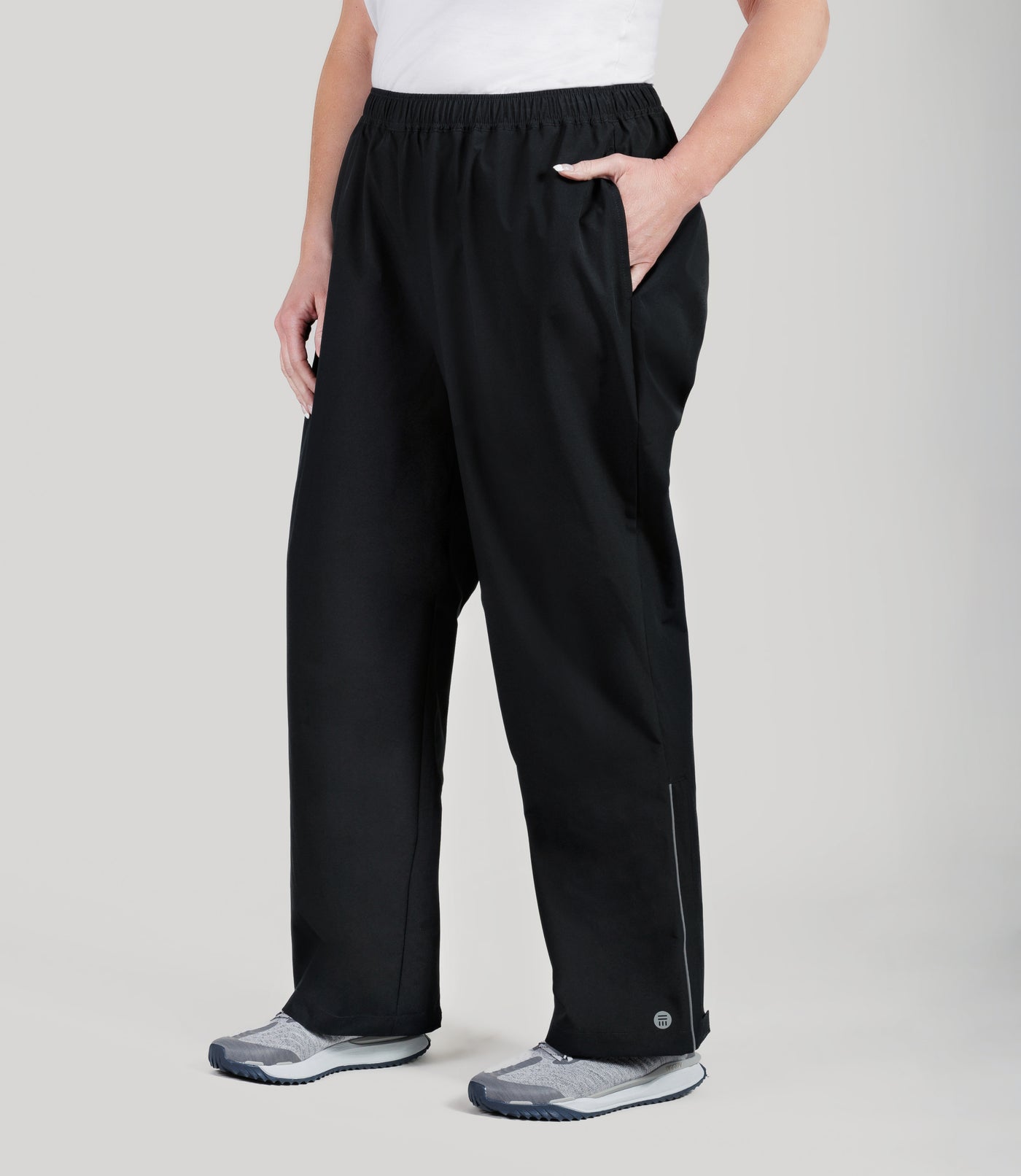 Plus size model, wearing JunoActive's Adventure Wind and Rain plus size pant in color black. Her left hand is in her pocket and right is draped by her side.