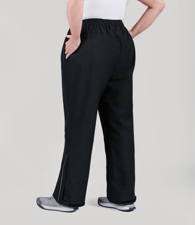 Plus size model, facing back, wearing JunoActive's Adventure Wind and Rain plus size pant in color black. Her left hand is in her pocket and right is on her hip.