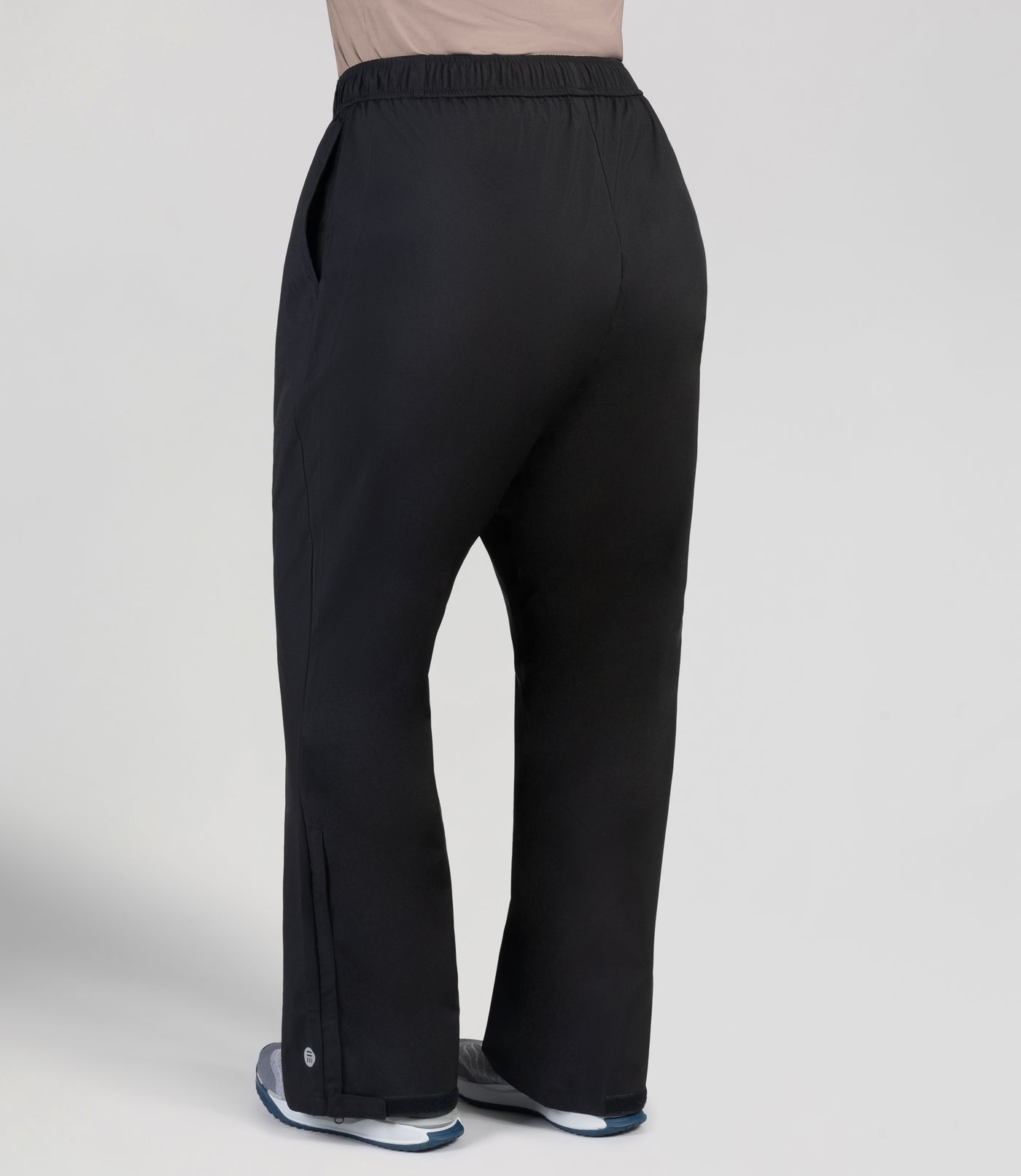 Bottom half of plus sized woman, facing back, wearing JunoActive Adventure Wind Rain Pant. These pants are full length and have pockets on each side in black.