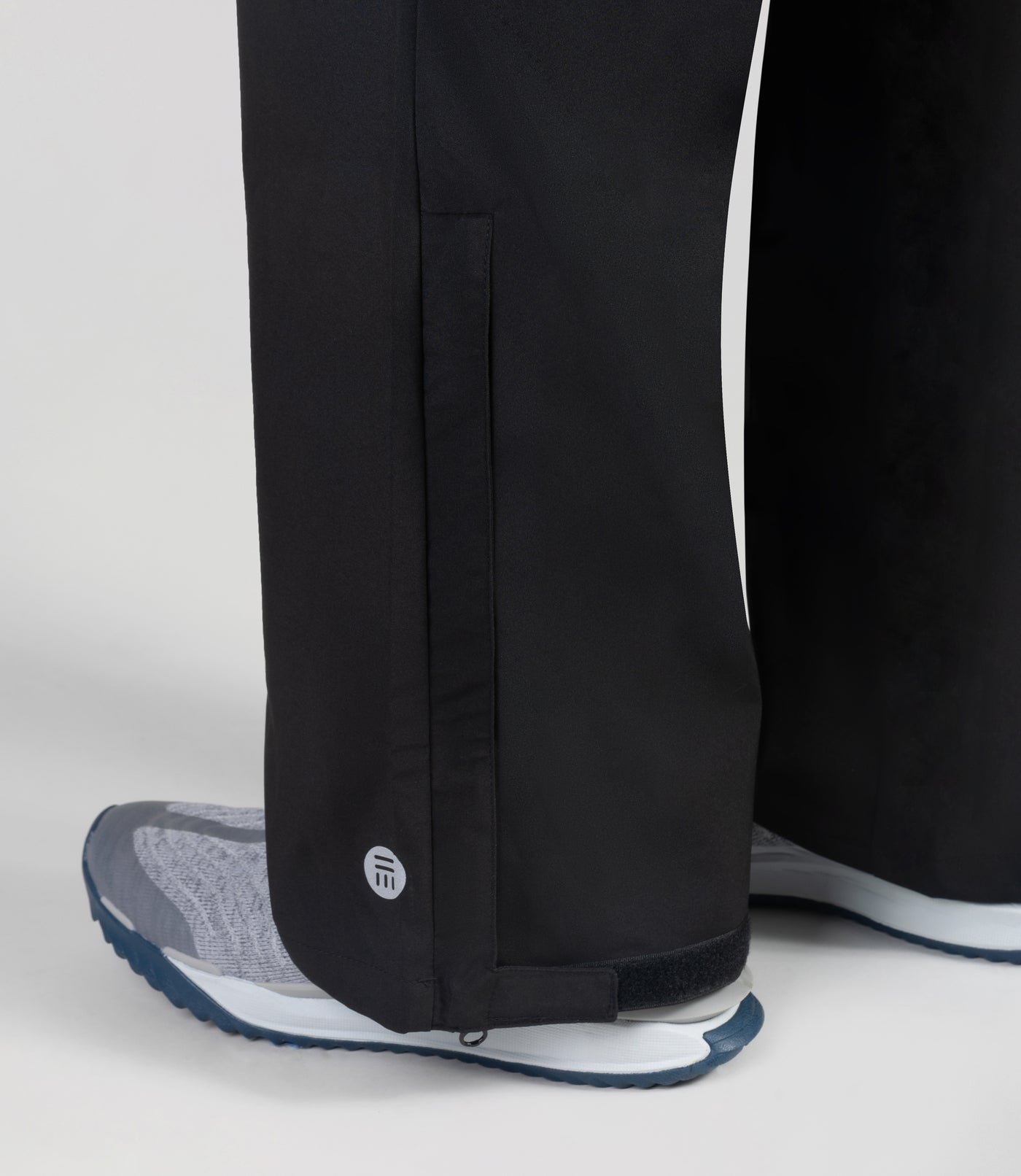 Close up of hems on pants of plus sized woman, facing back wearing JunoActive Adventure Wind Rain Pant. These pants are full length and have pockets on each side in black.