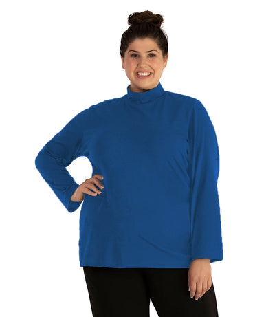 Plus size woman, facing front looking left, wearing JunoActive plus size Stretch Naturals Lite Mock Neck Top in the color Cozy Blue. She is wearing JunoActive Plus Size Leggings in the color Black.