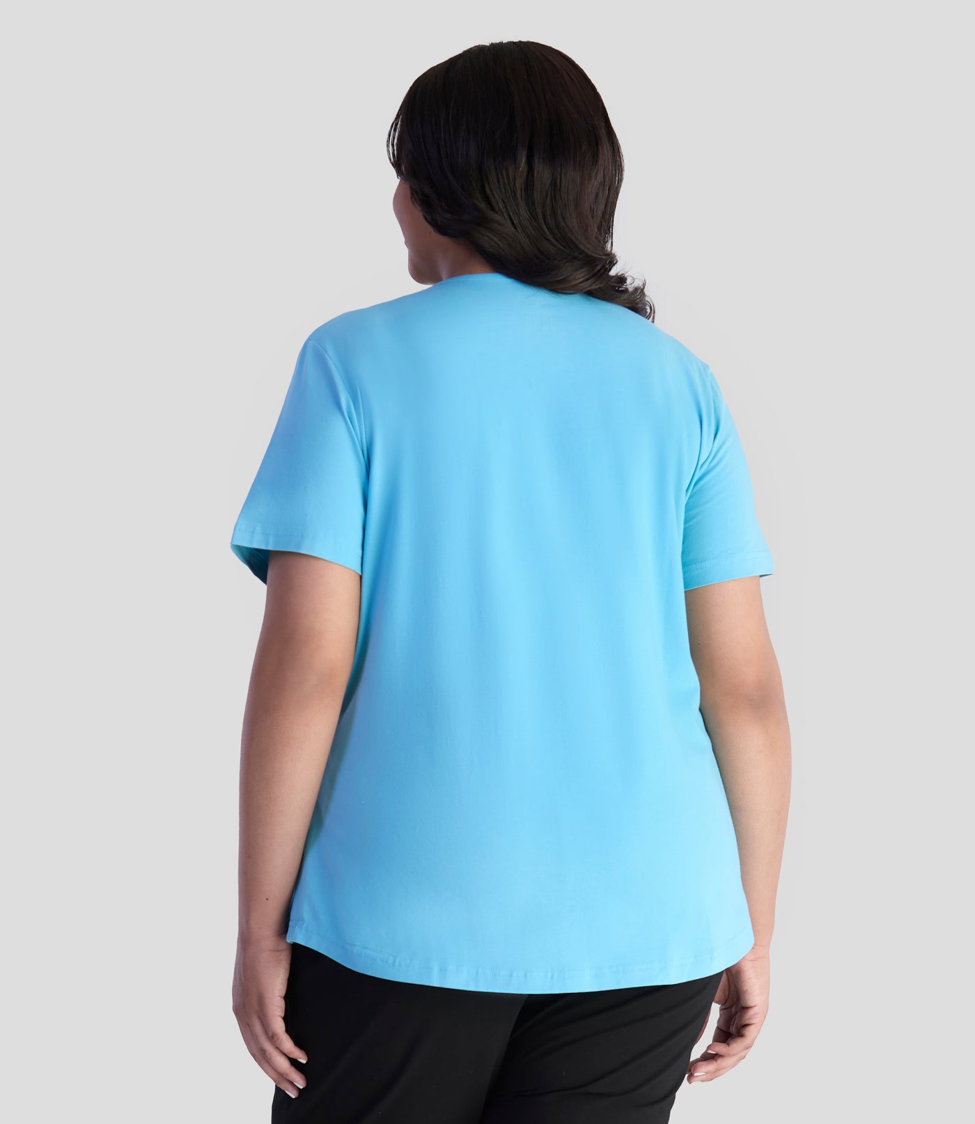 Model is facing back with her arms by her side. She is wearing JunoActive's Designer Graphic scoop neck top color mountain lake blue.