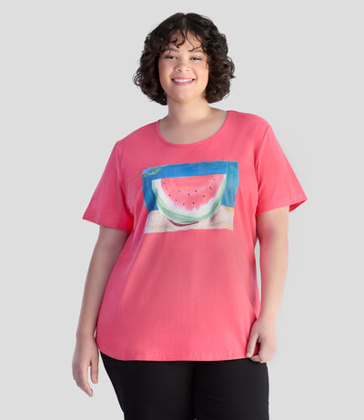 Model is facing forward with her arms by her side. She is wearing JunoActive's Designer Graphic scoop neck top with watermelon print on color carnation pink.