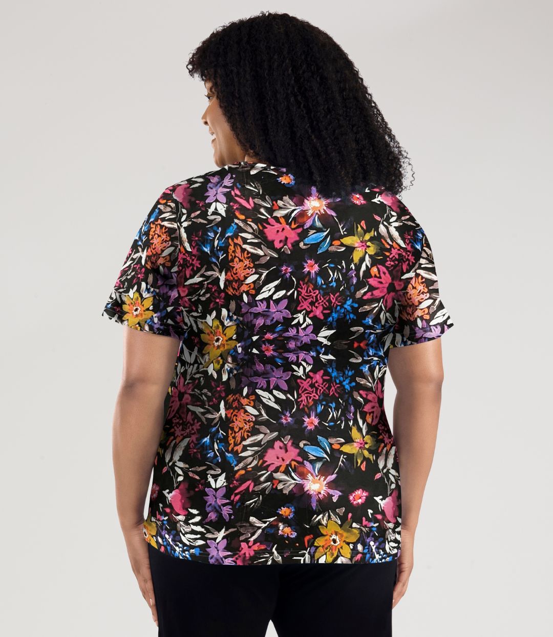 Model, facing back, wearing Junonia Lifestyle Printed Short Sleeve V-Neck top in floral forest print.