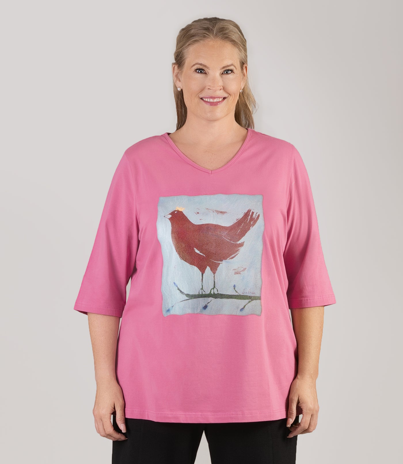 Plus size woman, facing front, wearing JunoActive’s Stretch Naturals Lite 3/4 Sleeve V-neck Tunic, color mulberry. Arms by side, chicken with a crown graphic.