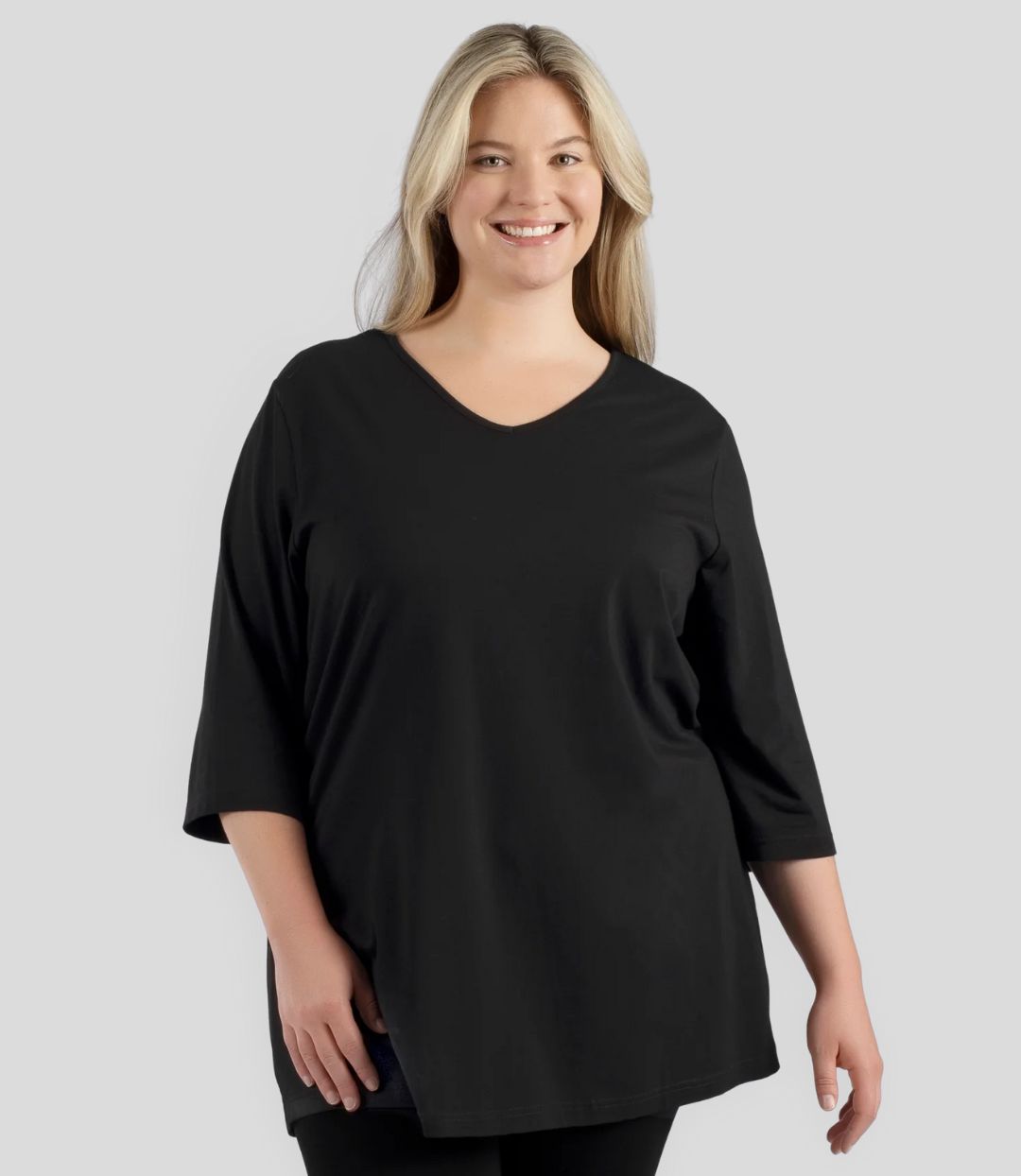 Plus size woman, facing front, wearing JunoActive’s Stretch Naturals Lite 3/4 Sleeve V-neck Tunic, color black. Arms by side.
