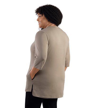 JunoActive Model wearing Stretch Naturals Lite 3/4 Sleeve Button Henley, facing back, one hand in pocket of shirt and other by her side. Color in Beachwood.