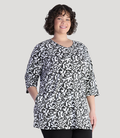 Model wearing JunoActive's Junonia Lifestyle Cotton Printed 3/4 sleeve pocket tunic in pattern black and white wildflower. Her right hand is in right pocket of shirt.