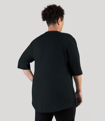 Plus size woman, facing back left, wearing JunoActive plus size Legacy Cotton Casual Tunic in the color  Black. She is wearing JunoActive Plus Size Leggings in the color black. 