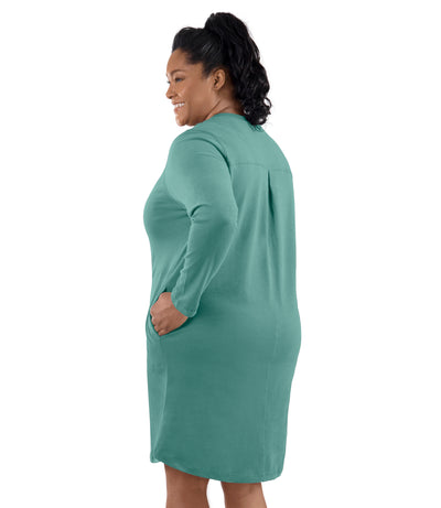 Plus-size model, facing back, left hand in dress pocket. Wearing JunoActive's Legacy Cotton Casual Pocketed Long Sleeve Dress in Lichen Green.