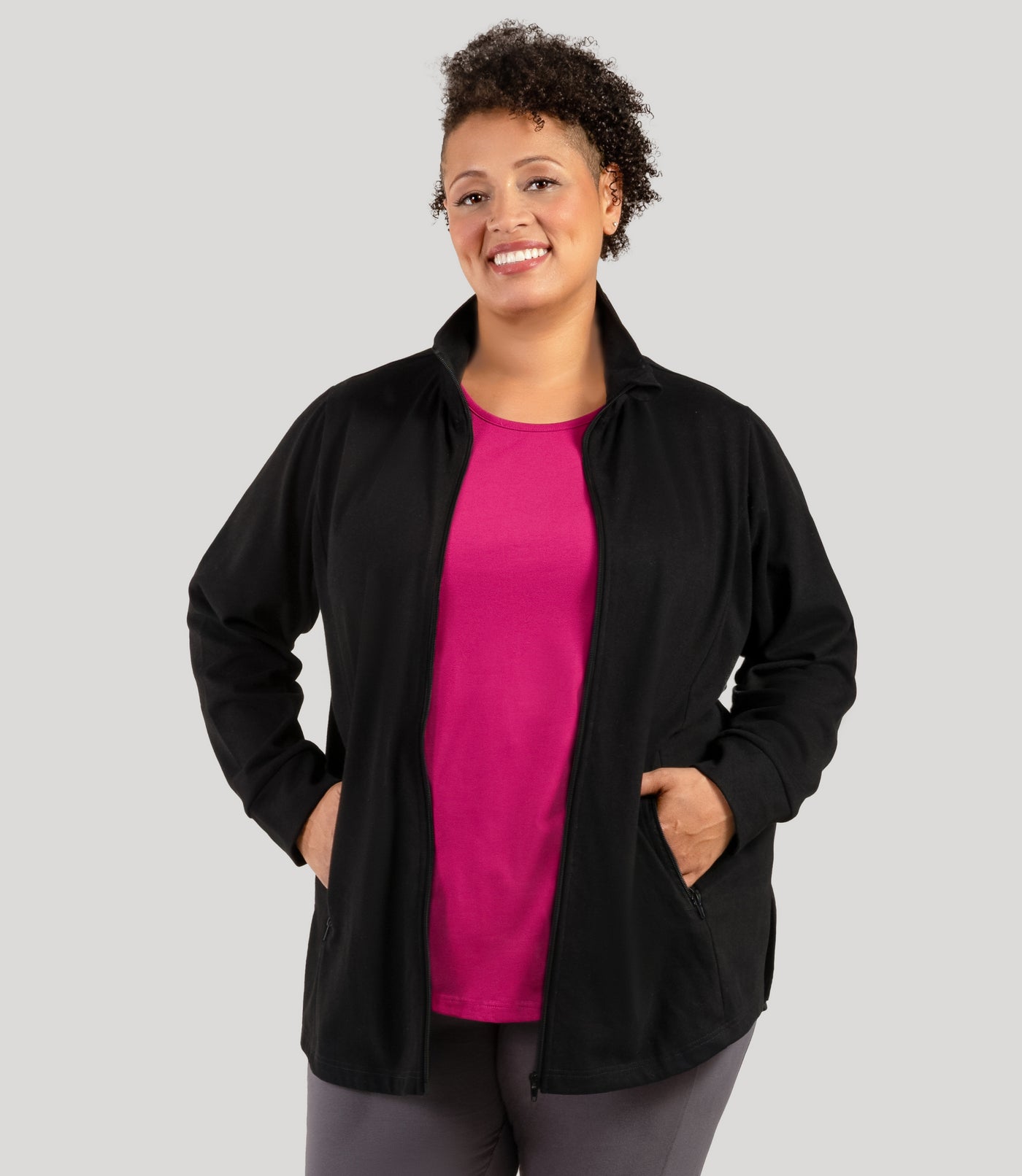 Plus size woman, facing front with hands in both pockets of jacket, wearing JunoActive's Legacy Cotton Casual Mock Neck Zip up plus size jacket in color black. Jacket is unzipped.