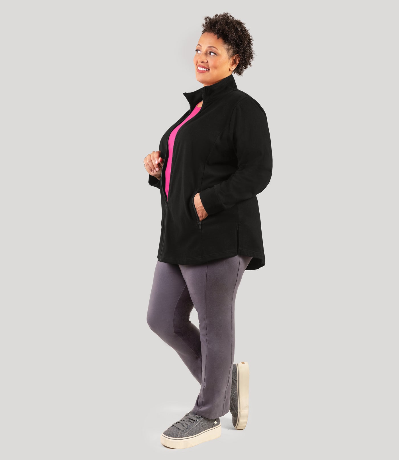 Plus size woman, facing side, wearing JunoActive's Legacy Cotton Casual Mock Neck Zip up in color black. Jacket is half zipped.