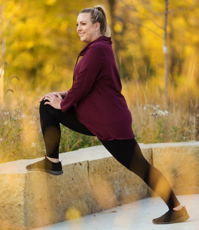 Plus size model, wearing Stretch Naturals Leggings, and long sleeve JunoActive top at a park, stretching, preparing for a walk.