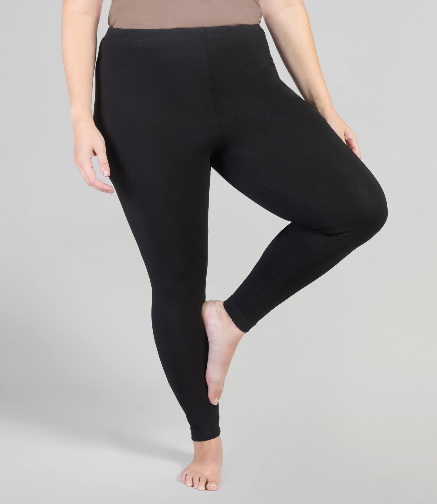 Bottom half of plus sized woman, front view with left leg up resting on right calf, wearing JunoActive Stretch Naturals Leggings in color black. Bottom hem is at the ankle. 