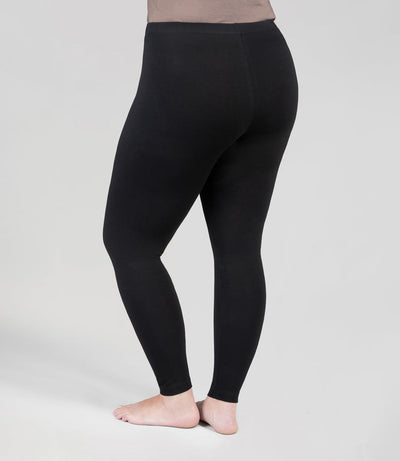 Bottom half of plus sized woman, back view with left leg up resting on right calf, wearing JunoActive Stretch Naturals Leggings in color black. Bottom hem is at the ankle. 