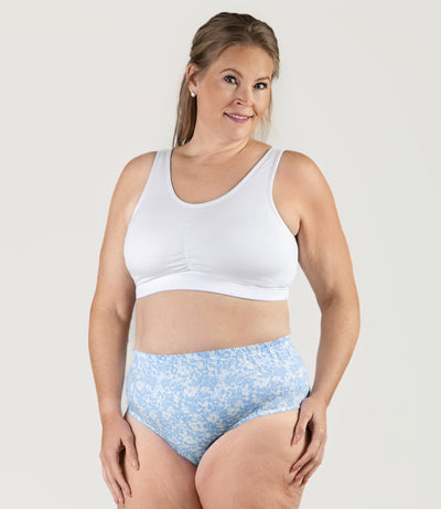 Plus size woman, facing to the front, both hands by side, wearing JunoActive Stretch Naturals Shirred plus size Bra Top. Plus size bra is gathered in middle and has a scoop neck. Straps are wide and bra color is white.