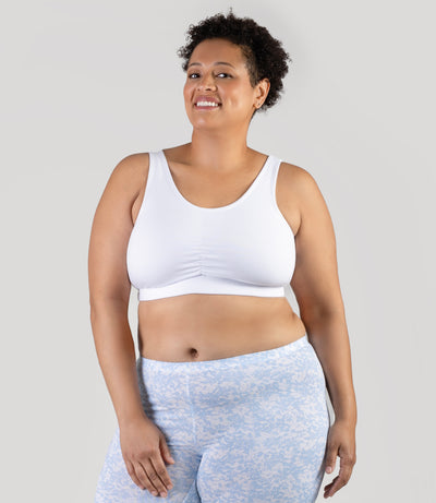 Plus size woman, facing to the front, both hands by side, wearing JunoActive Stretch Naturals Shirred plus size Bra Top. Plus size bra is gathered in middle and has a scoop neck. Straps are wide and bra color is white.