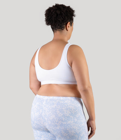 Plus size woman, facing to the back, both hands by side, wearing JunoActive Stretch Naturals Shirred plus size Bra Top. plus size sports Bra is gathered in middle front and has a scoop neck and back. Straps are wide and bra color is white.