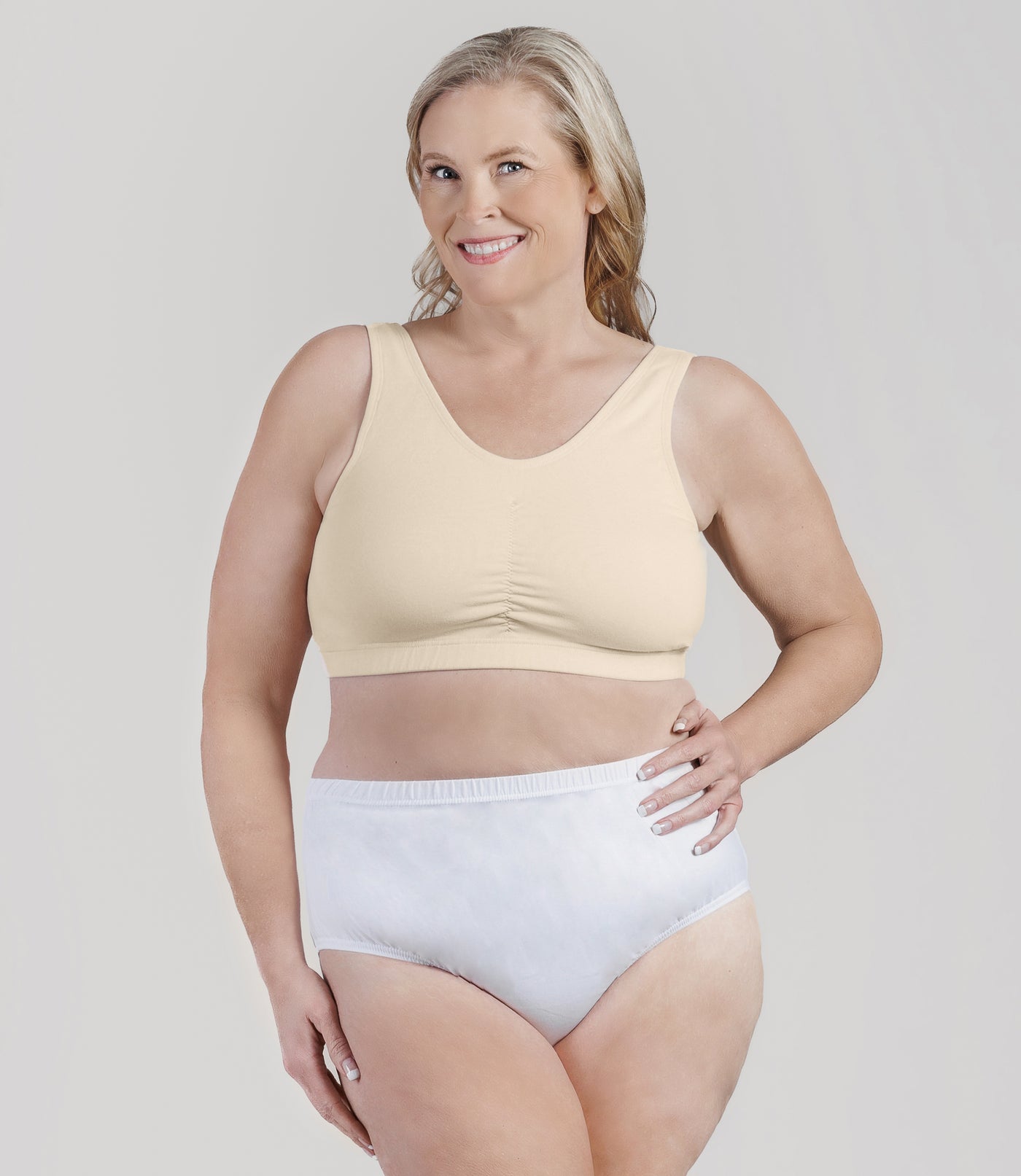 Plus size woman, facing front, wearing JunoActive Stretch Naturals Shirred Bra Top. Bra is gathered in middle and is a scoop top neck. Straps are wide and bra color is sandy.