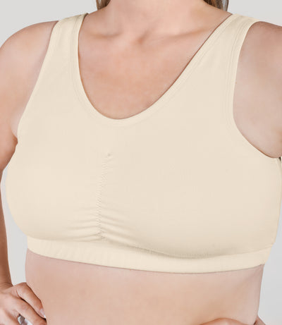 Close up of plus size woman, facing front, wearing JunoActive Stretch Naturals Shirred Bra Top. Bra is gathered in middle and is a scoop top neck. Straps are wide and bra color is sandy.