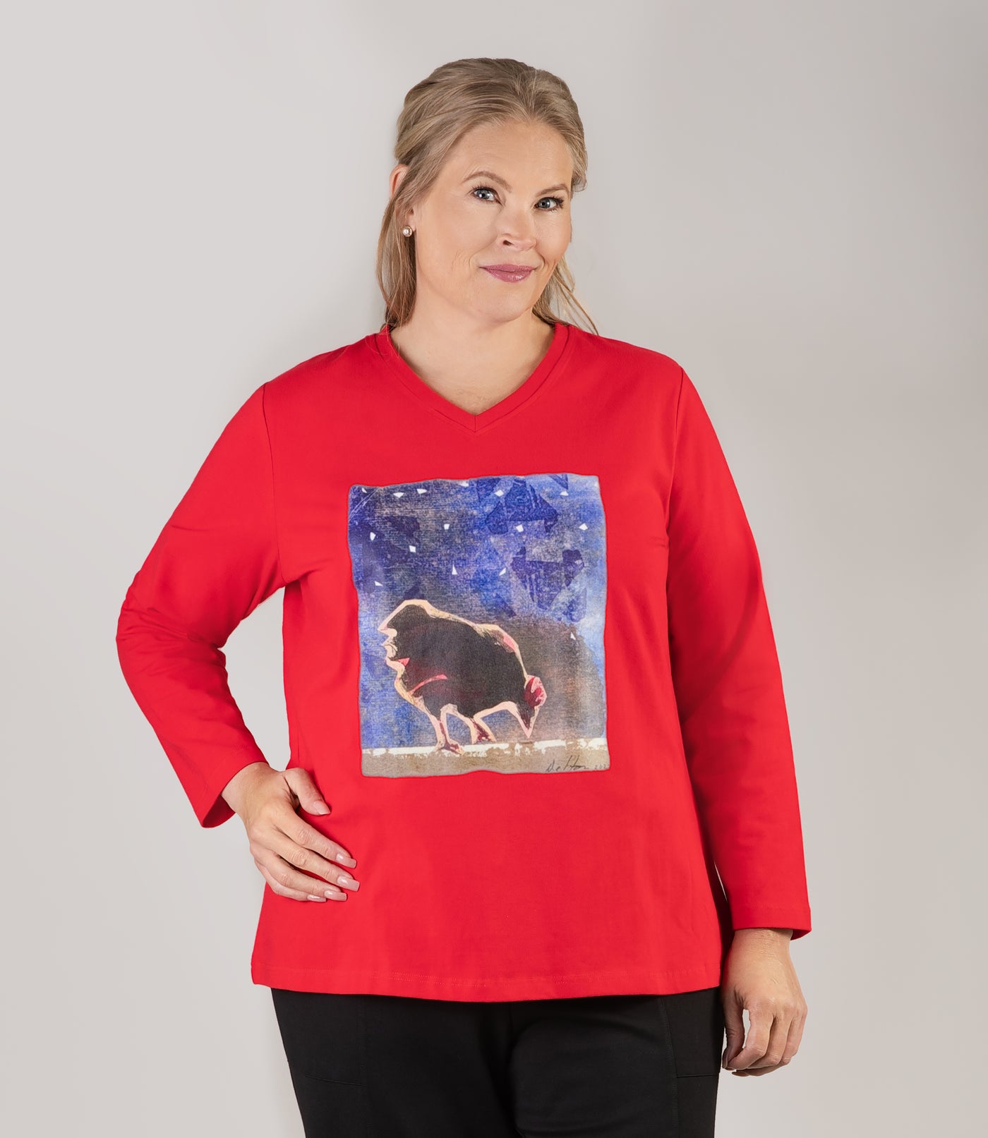 Plus size woman, facing front looking straight, wearing JunoActive plus size Stretch Naturals Long Sleeve V-Neck Top in the color Lucky Red with a designer graphic of a rooster with a nighttime sky. She is wearing JunoActive Plus Size Leggings in the color Black.