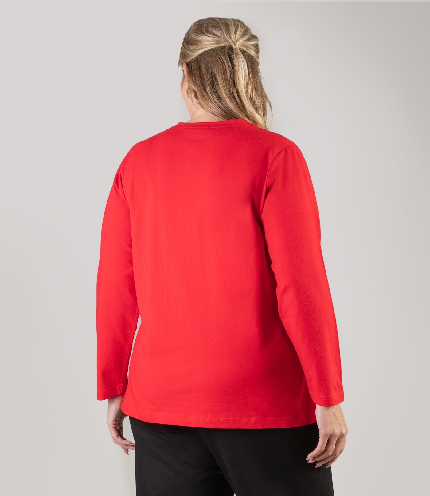 Plus size woman, facing back looking to the left with her arms by her side, wearing JunoActive plus size Stretch Naturals Long Sleeve V-Neck Top in the color Lucky Red. She is wearing JunoActive Plus Size Leggings in the color Black.