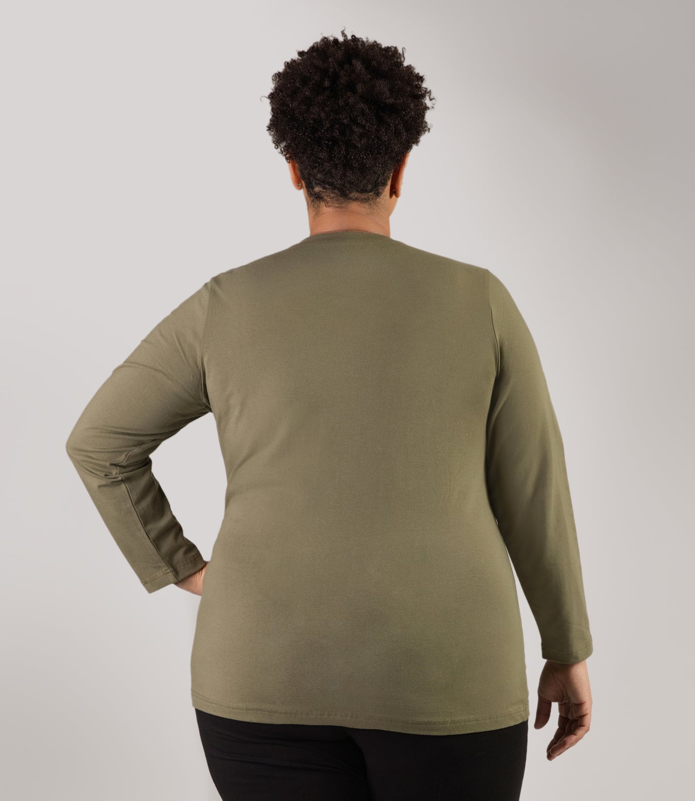 Plus size woman, facing back looking straight, wearing JunoActive plus size Stretch Naturals Long Sleeve V-Neck Top in the color Moss Green. She is wearing JunoActive Plus Size Leggings in the color Black.