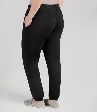 Bottom half of plus sized woman, back view, wearing junoactives stretch naturals jogger pockets black. The pants are full length and have pockets on each side.