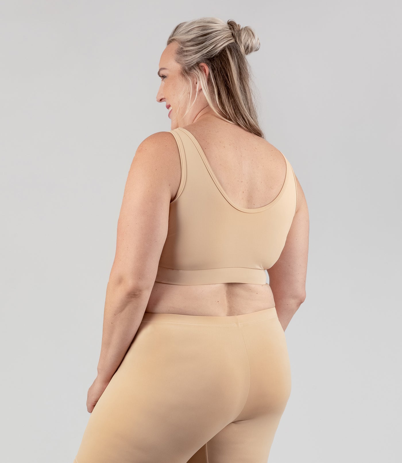 Plus size woman, facing back, wearing JunoActive plus size Junowear Hush V-Neck Bra in Ecru. The woman is wearing a ecru Junowear Hush Boxer brief. Her arms fall naturally to her side.