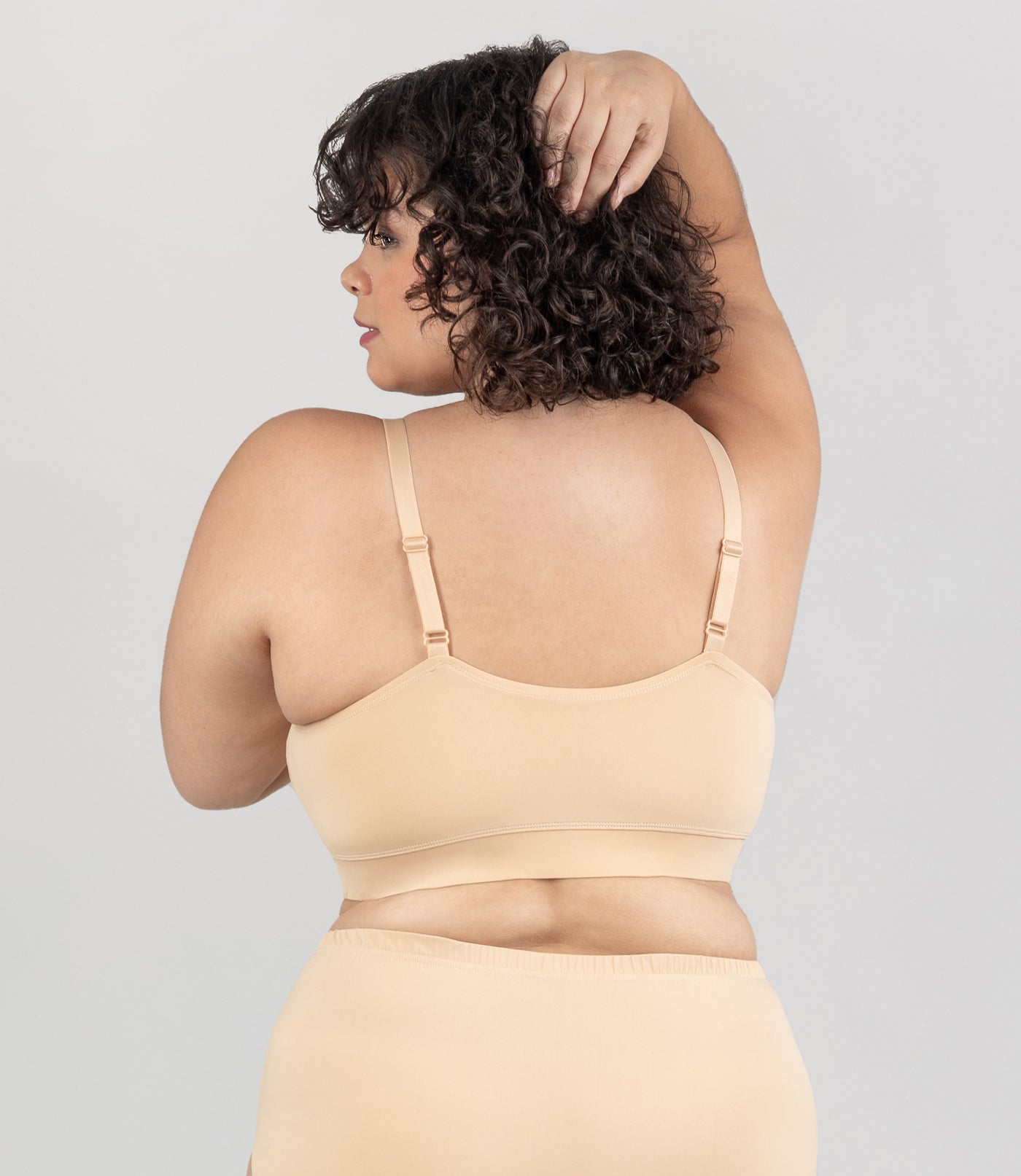 Plus size model wearing JunoActive's Junowear Hush adjustable bralette in color ecru. Model is facing back with her head turned at profile.