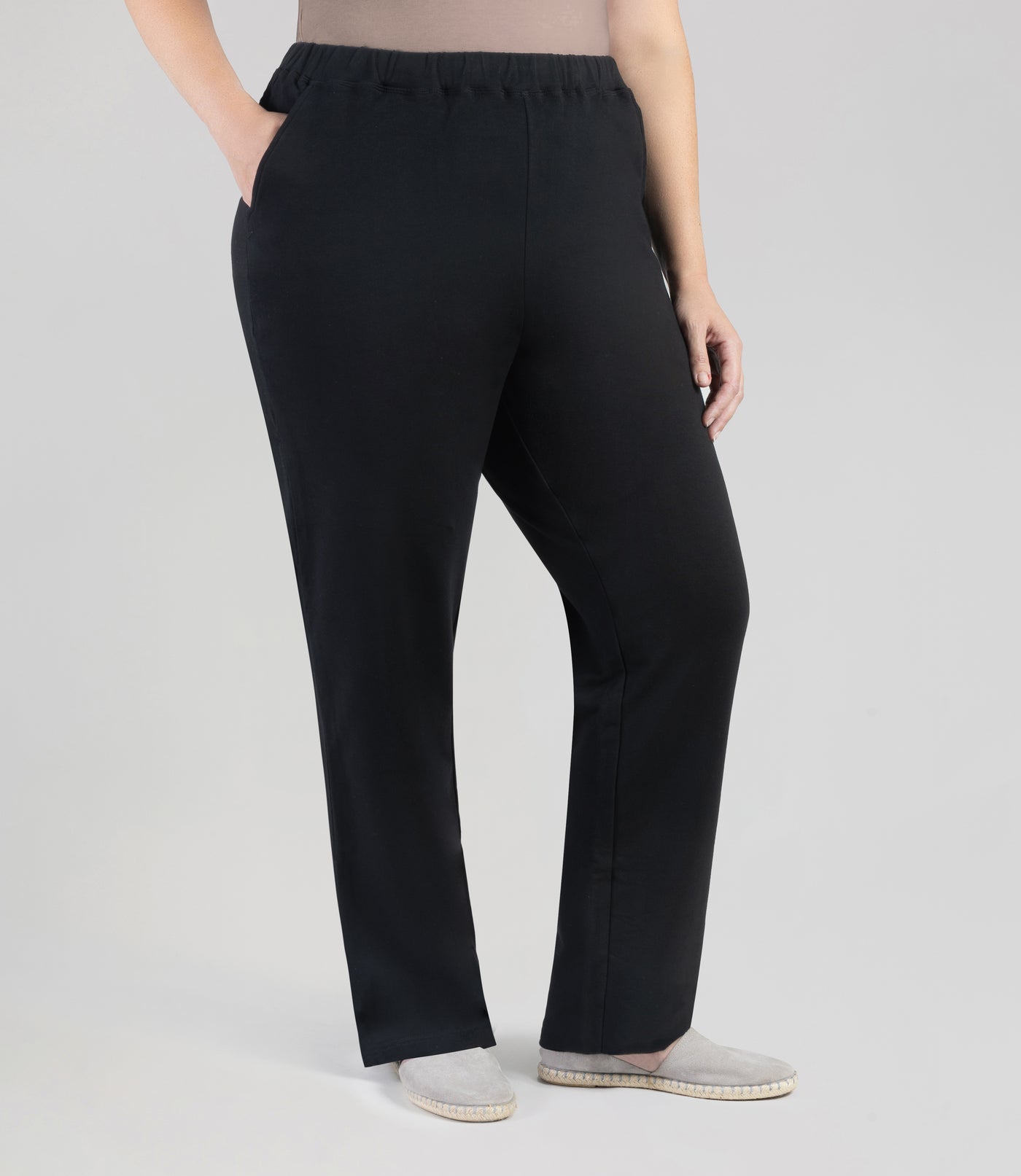 Plus size woman facing front, wearing JunoActive's MaVie Pocketed Pant in black. One hand is in pocket and other is by side.
