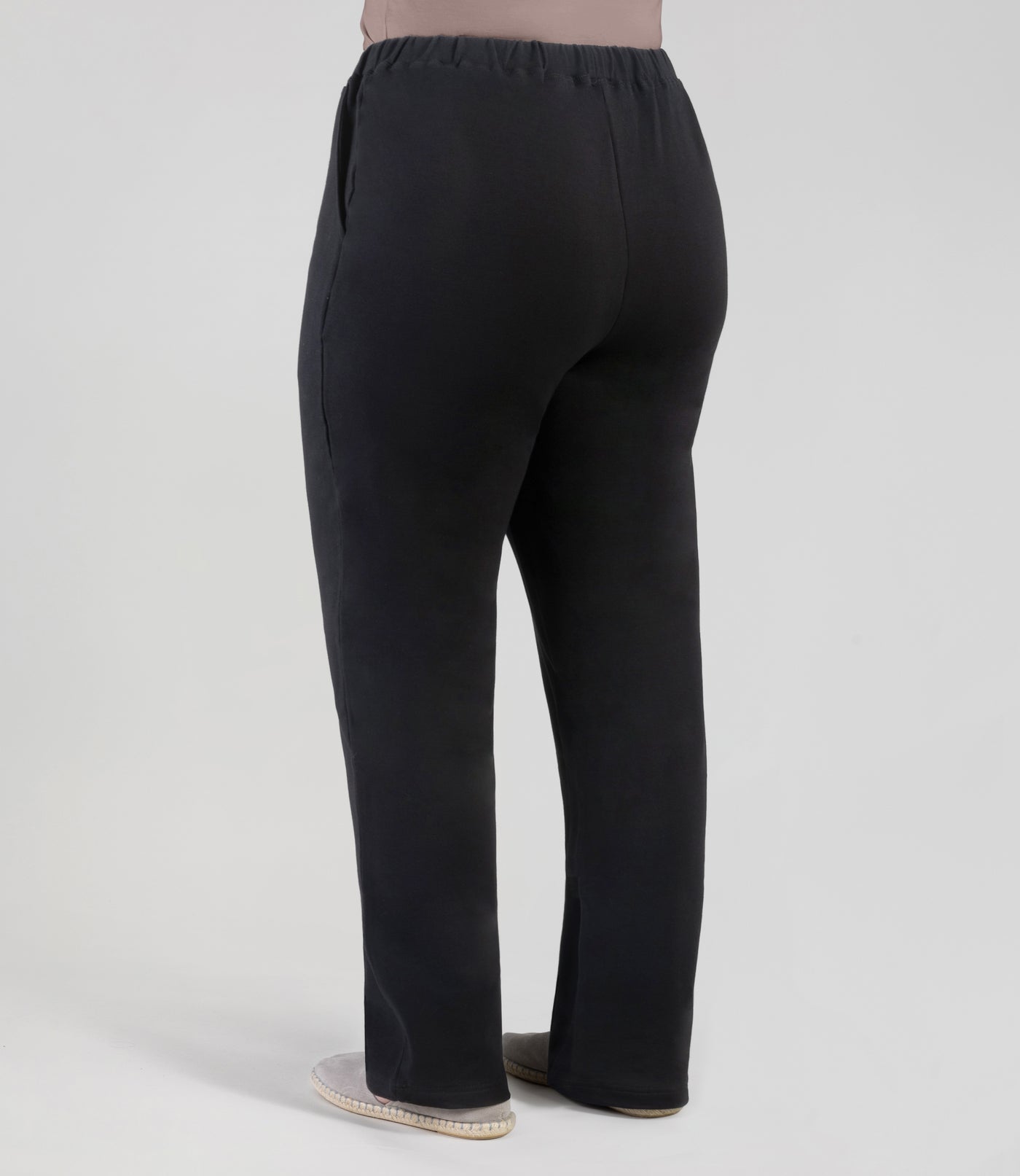 Plus size woman facing back, wearing JunoActive's MaVie Pocketed Pant in black. One hand is in pocket and other is by side.