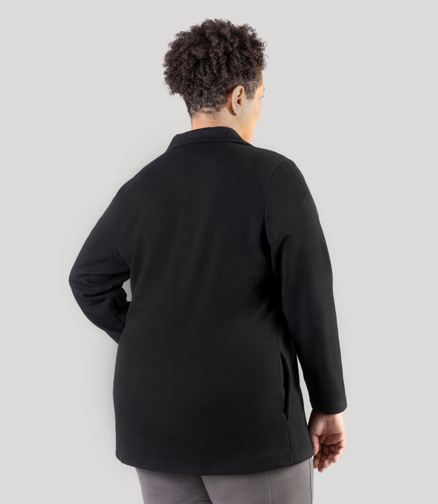 Plus size model, facing back, wearing JunoActive's JunoWaffle Cotton Long Sleeve Button top with her left hand on her left hip and right hand by her right side.