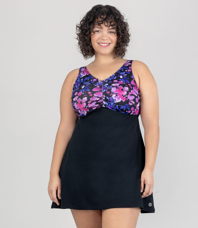 JunoActive model wearing Aquasport Shirred Swim Dress. Top of dress is pink and blue floral elegance print and under bust is black fabric. Bust has shirred down the middle to create a lovely shape.
