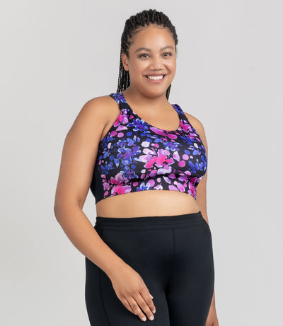 JunoActive model, facing front, wearing Aquasport Hanalei Bra Top featuring blue and pink floral elegance print. Model facing front with her right hand resting on her right leg. Left arm is to her left side. 